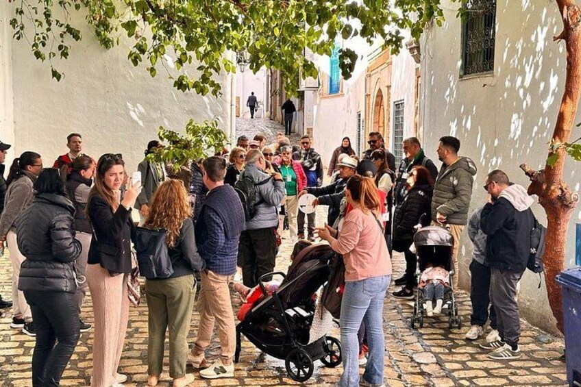 A group of people gathered on a cobblestone street, some standing and others sitting on a bench. 2