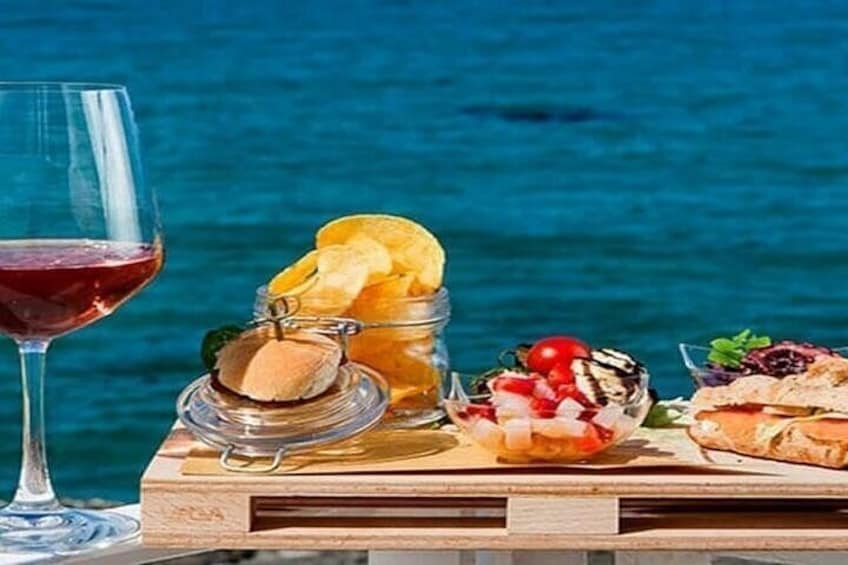 A wooden table with a glass of red wine, a jar of pickles, a bowl of salad, and a sandwich. 5