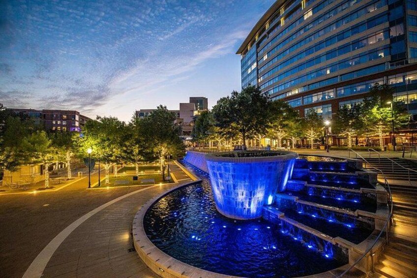 A nighttime urban scene with a water feature, illuminated steps, and surrounding buildings. 2
