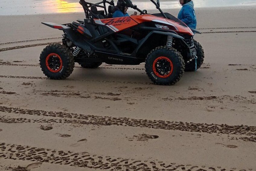 A red and black off-road vehicle on a sandy beach with footprints leading away from it. 3