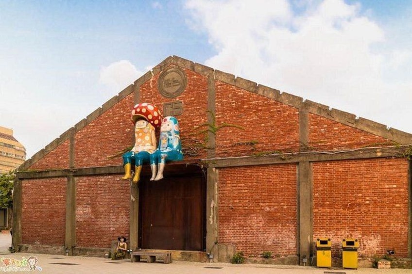 Un bâtiment en briques doté d’une grande porte et orné d’une fresque représentant deux personnages sur un champignon. 2