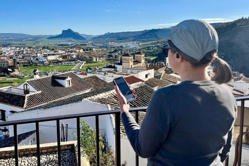 A person using a smartphone, overlooking a town with historical buildings and a mountain in the background. 2