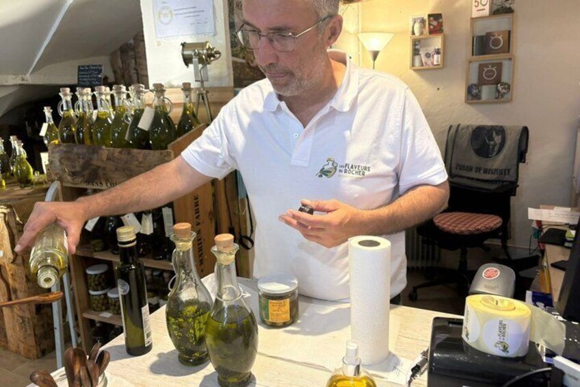 A man in a white shirt with a logo, standing at a table with various bottles and a roll of paper towels. 1