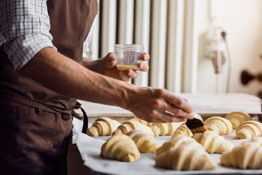 Una persona con delantal sirve croissants y un vaso de líquido. 2