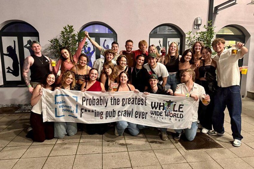 A group of people holding a banner in front of a building with arched windows. 3