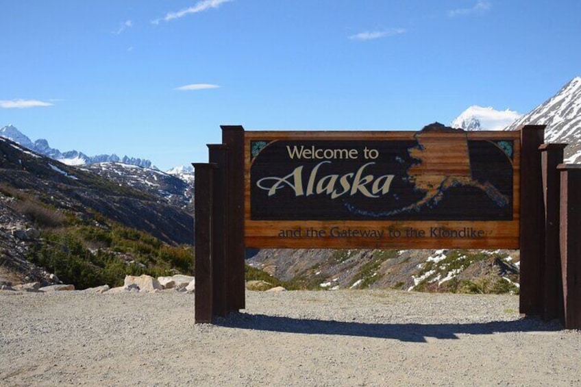 A wooden welcome sign for Alaska with a mountainous backdrop. 5