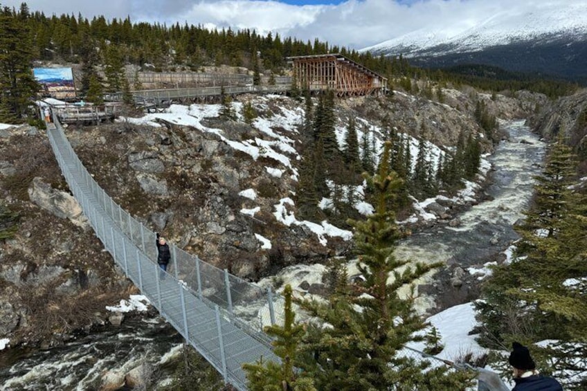 A suspension bridge over a river, surrounded by snow-covered mountains and trees. 2