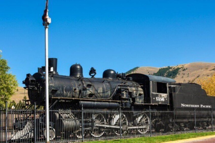 A vintage steam locomotive with 'Northern Pacific' written on the side, parked on tracks with a clear blue sky and hills in the background. 3