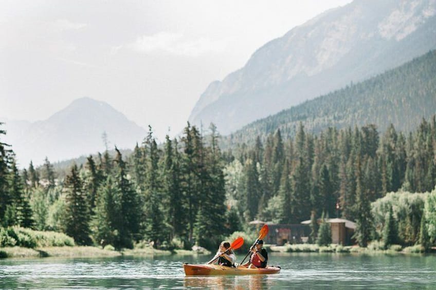 Two people kayaking on a calm river surrounded by dense forest and mountains. 3
