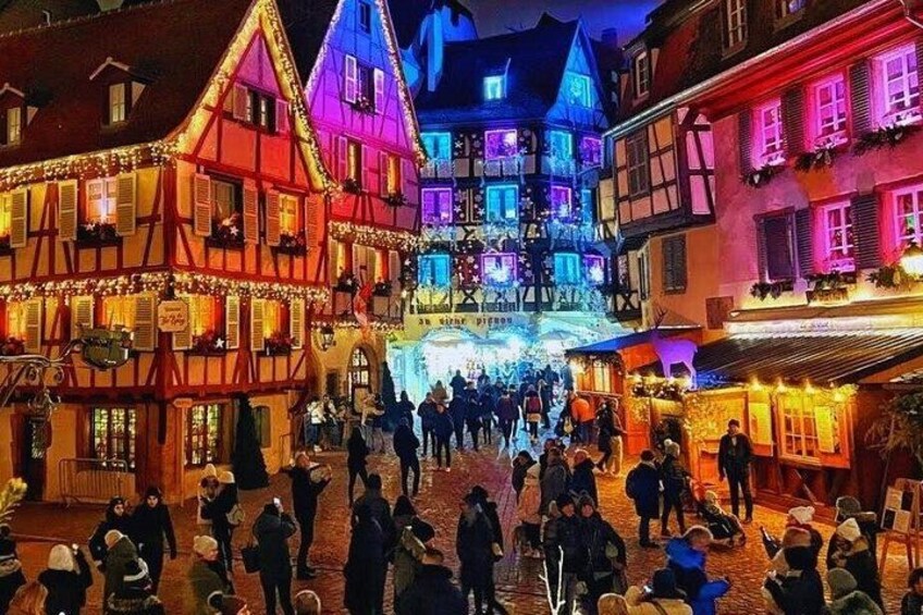 Una calle medieval iluminada con edificios coloridos y una multitud de personas. 1