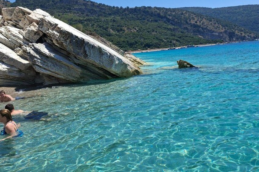 Clear turquoise sea, rocky coastline, and a forested hill in the background. 4