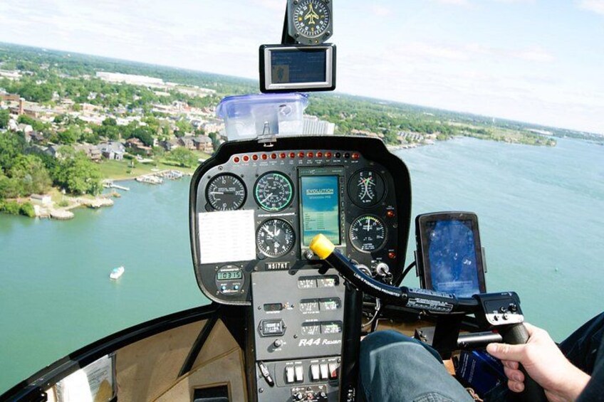 A helicopter cockpit with a view of a river and a town below. 2
