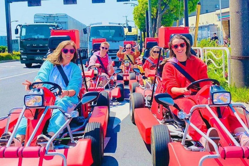 Des personnes conduisent des karts rouges sur une route, avec des camions en arrière-plan. 2
