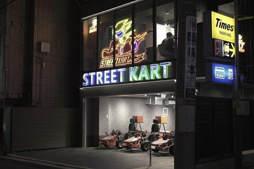 A brightly lit storefront with neon signs for 'Street Kart' and 'Times Parking.' 2