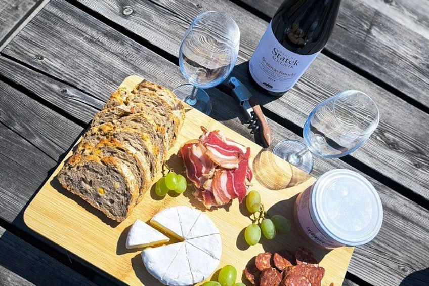 A wooden table with a charcuterie board, including sliced meats, cheese, grapes, and a loaf of bread. A bottle of wine and glasses are also visible. 2