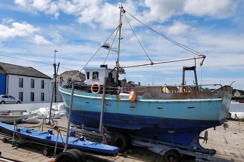 En blå og hvid båd på en trailer, fortøjet i en havn med bygninger og en bil i baggrunden. 4