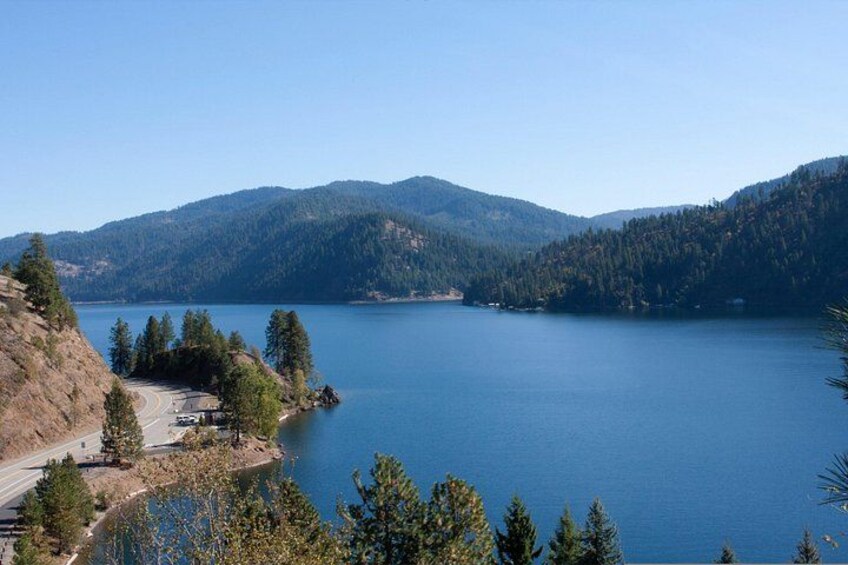 A lake surrounded by mountains, a road, and trees. 4