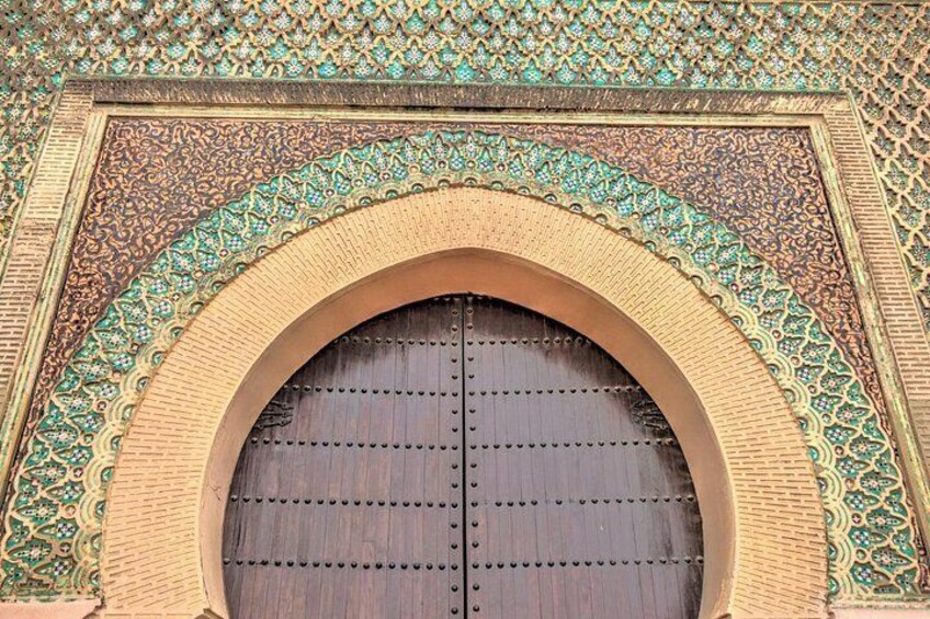 A large wooden door with intricate geometric patterns and a decorative archway. 1