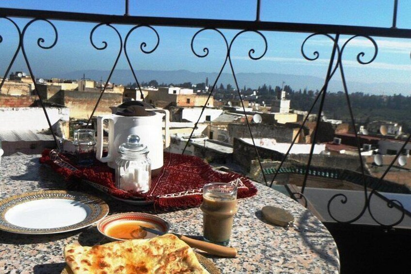 A table with a teapot, cups, and food on a balcony overlooking a cityscape. 3