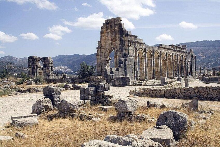 Ancient ruins with stone columns and arches, surrounded by dry grass and rocks. 5