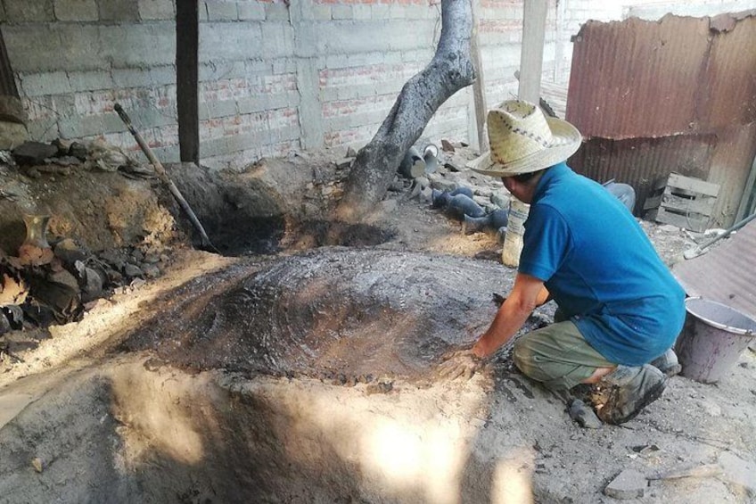 A person working with a large, round, dark object on a dirt ground, surrounded by construction materials and a partially constructed building. 2