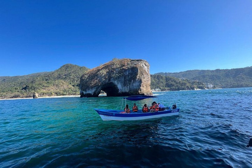 Un bote con pasajeros en un día despejado, una gran formación rocosa al fondo y agua tranquila. 5