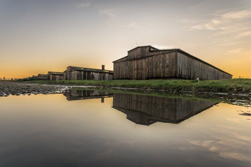 Un grand bâtiment en bois qui se reflète dans une étendue d’eau calme, entouré de prairies et sous un ciel dégagé. 4