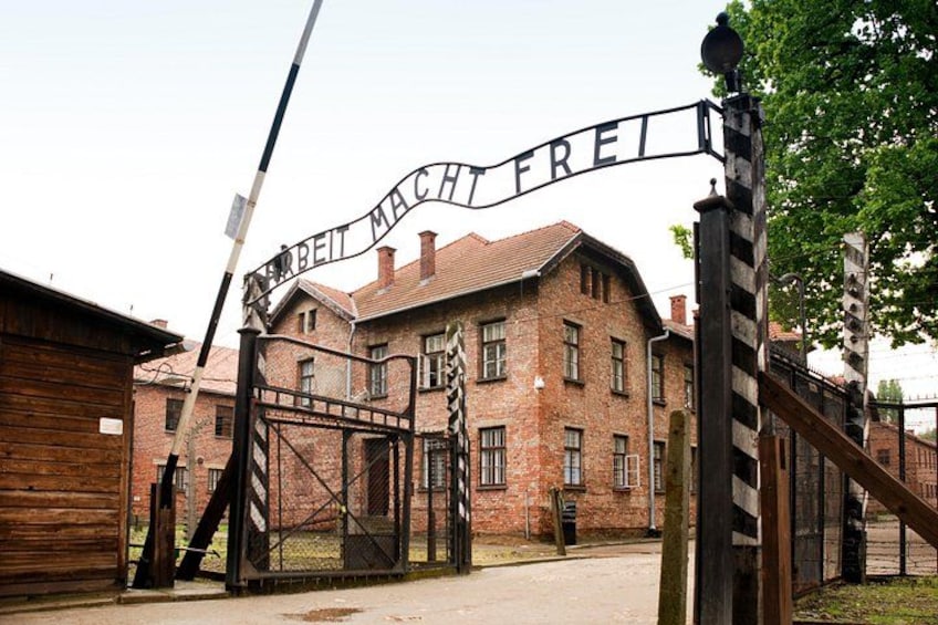 En murstensbygning med et skilt, der siger 'Arbeit Macht Frei', og en port med et stribemønster. 2