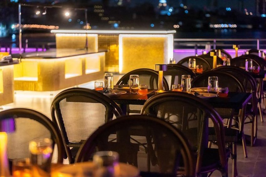 Un ristorante all'aperto con tavoli e sedie, una zona bar e luci cittadine sullo sfondo. 2