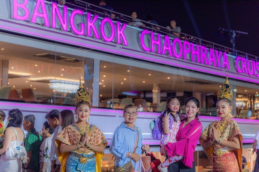 A group of people in traditional attire in front of a brightly lit building with 'BANGKOK' and 'CHAOPHRAYA CRUIS' signage. 3