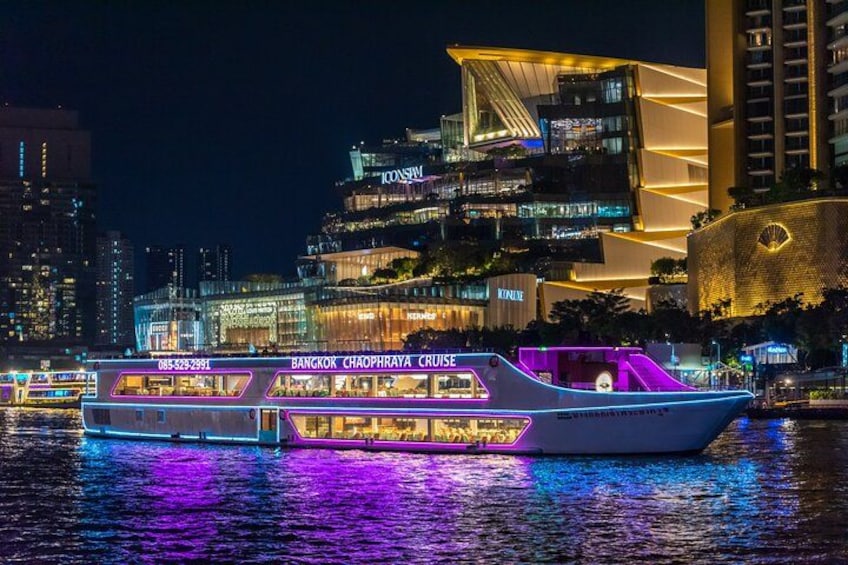 A brightly lit boat with neon lights on a river, with modern buildings in the background. 1