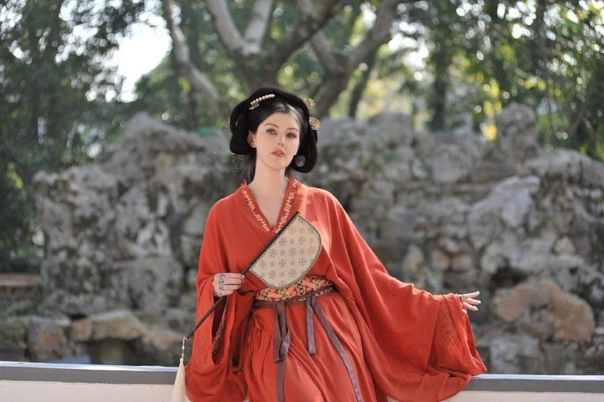 A person in traditional attire holding a fan, standing in front of a rocky landscape. 1