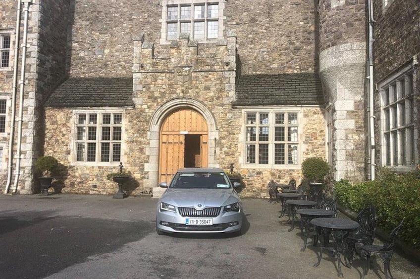 A stone building with a car parked in front, outdoor tables, and chairs. 2