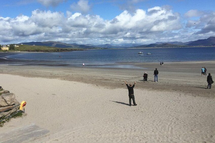 A sandy beach with people, a calm sea, and distant mountains. 1