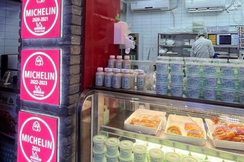 Een bakkerij met een vitrine vol gebak en een bord met een Michelin-ster. 4
