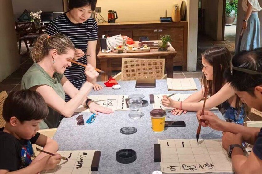 Un grupo de personas participa en una clase de caligrafía, con herramientas y papel sobre la mesa. 1