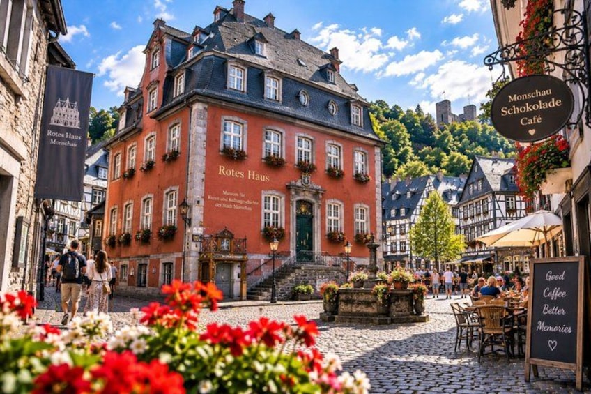 A cobblestone street with a red building labeled 'Rotes Haus' and a café named 'Monsehauf Schokolade Café'. 3