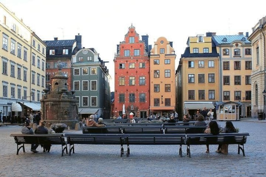 Ein Kopfsteinpflasterplatz mit bunten Gebäuden, Bänken und einem Brunnen. 4