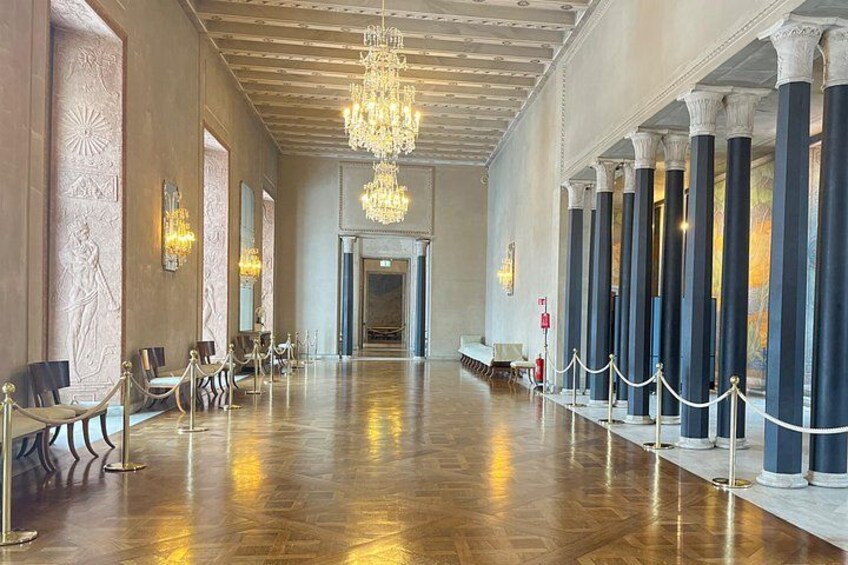 A grand hallway with a polished wooden floor, ornate columns, and a chandelier. 3