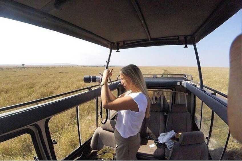 A person in a vehicle with a camera, looking out at a flat landscape. 5