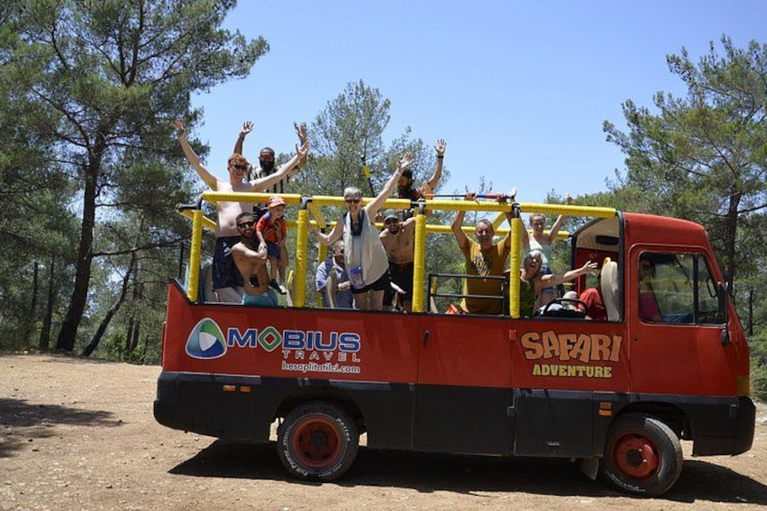A safari adventure vehicle with people on top, surrounded by trees. 1