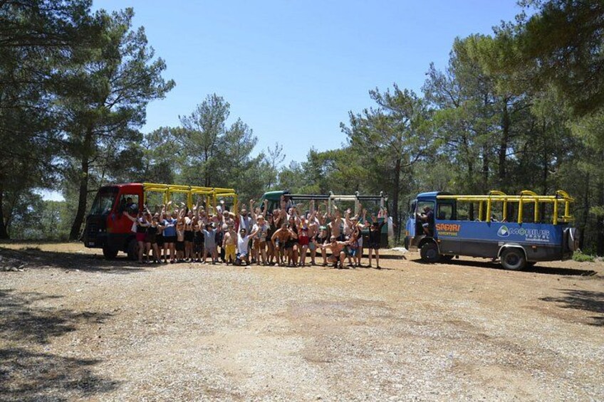 A group of people gathered outdoors, with a dirt ground and trees in the background. 5