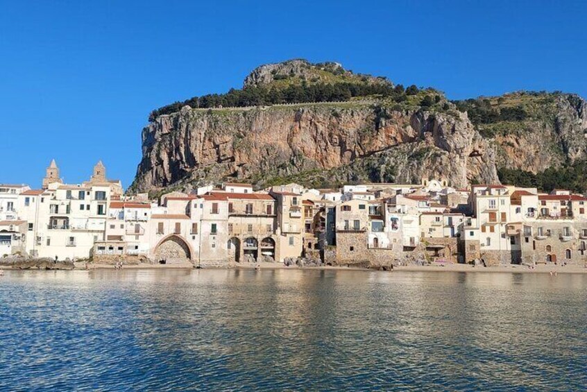 A coastal town with buildings along the waterfront, a prominent cliff, and a clear blue sky. 1