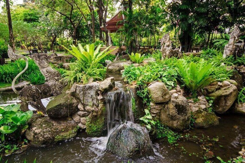 A waterfall cascading over rocks in a lush garden with tropical plants and a traditional building in the background. 4