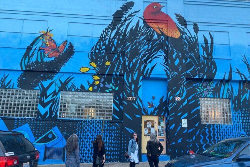 Un mural con un pájaro, flores y diseños abstractos en una edificación. 4