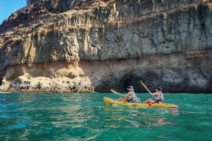Two people kayaking on turquoise water with rocky cliffs in the background. 1