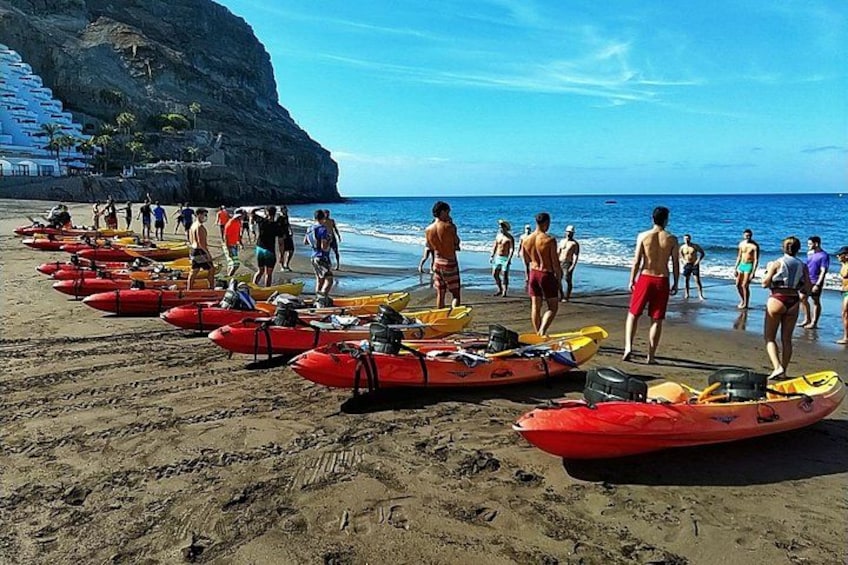A beach with red kayaks lined up, people walking, and a cliff in the background. 4