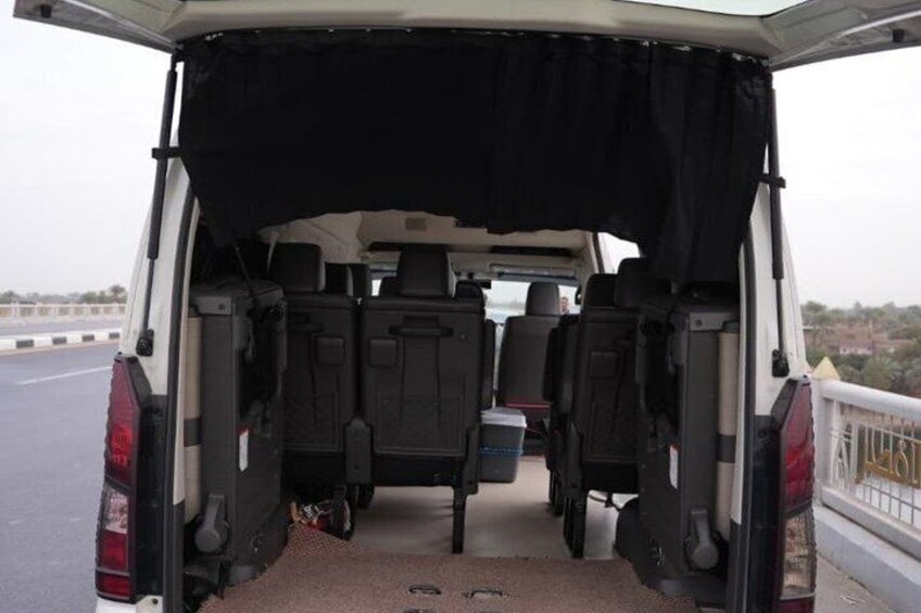 The back of a white van with an open cargo area, two black seats, and a black cover over the cargo. 2
