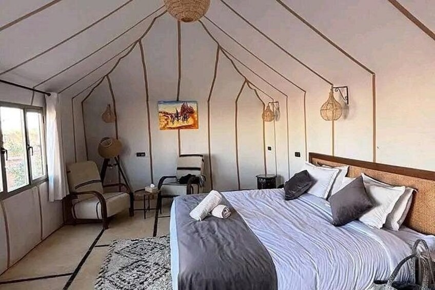 A tented accommodation with a bed, chairs, a table, and wall art. 3