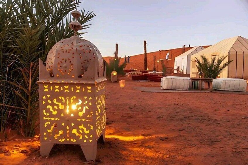 A desert landscape with a white lantern, palm trees, and a building in the background. 4
